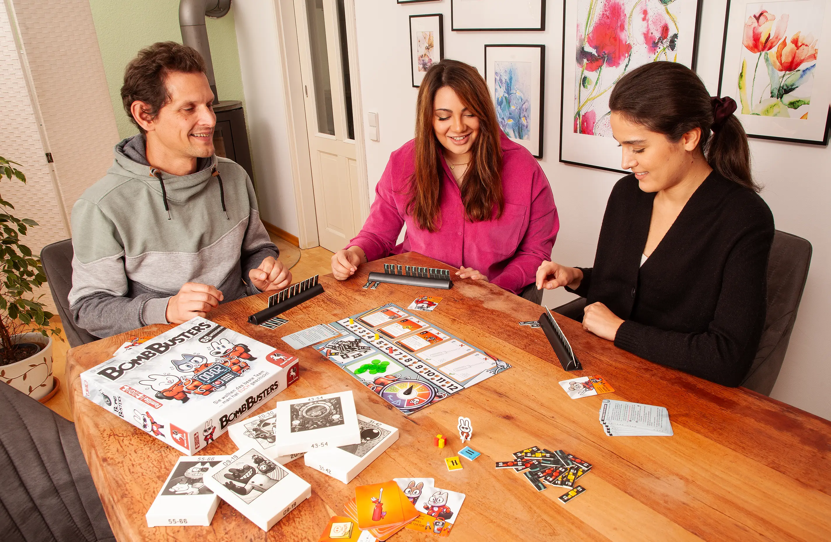 Drei Personen sitzen an einem Tisch und spielen das Brettspiel Bomb Busters