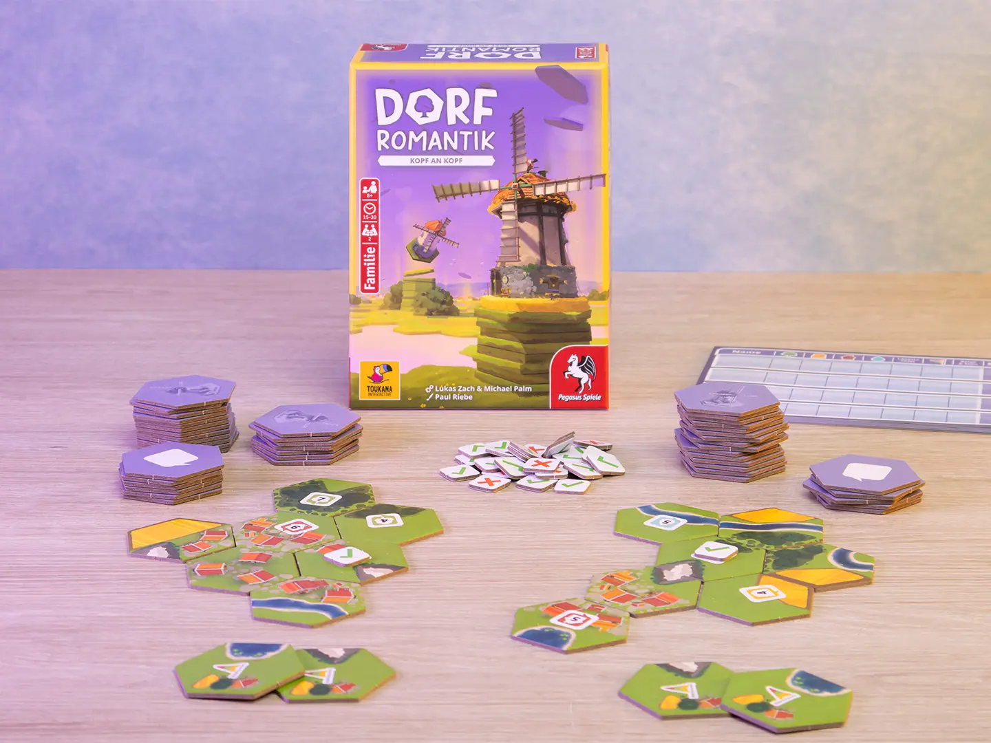 Spielschachtel von Dorfromantik – Kopf an Kopf mit zwei ausgelegten Landschaften aus sechseckigen Plättchen, mehreren Plättchenstapeln und Spielmarkern auf einem Holztisch
