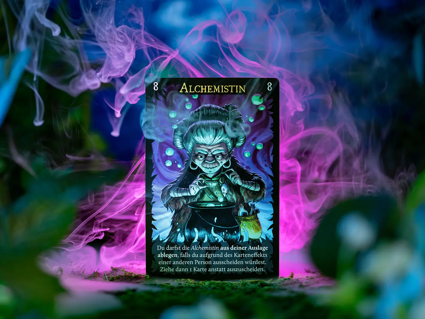Spielkarte Alchemistin aus Wolfsmond mit einer älteren Frau, die über einem Kessel einen Trank zubereitet, umgeben von violettem und türkisfarbenem Rauch.