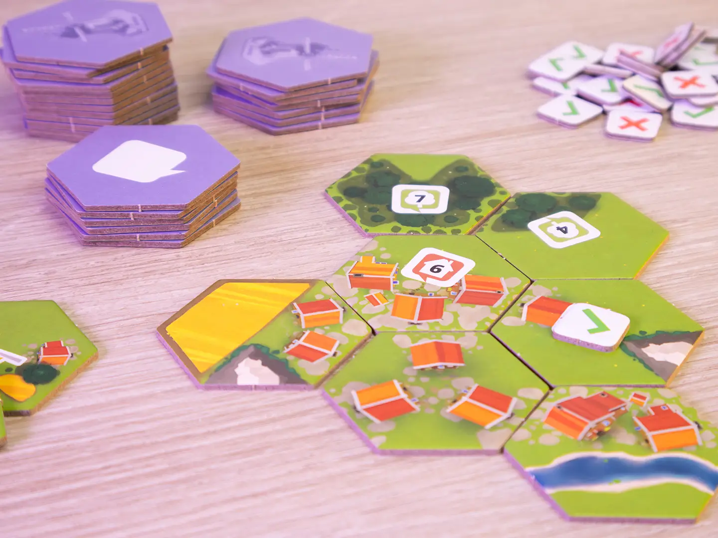 Mehrere Landschaftsplättchen mit Wiesen, Wäldern und Gebäuden aus dem Brettspiel Dorfromantik – Kopf an Kopf