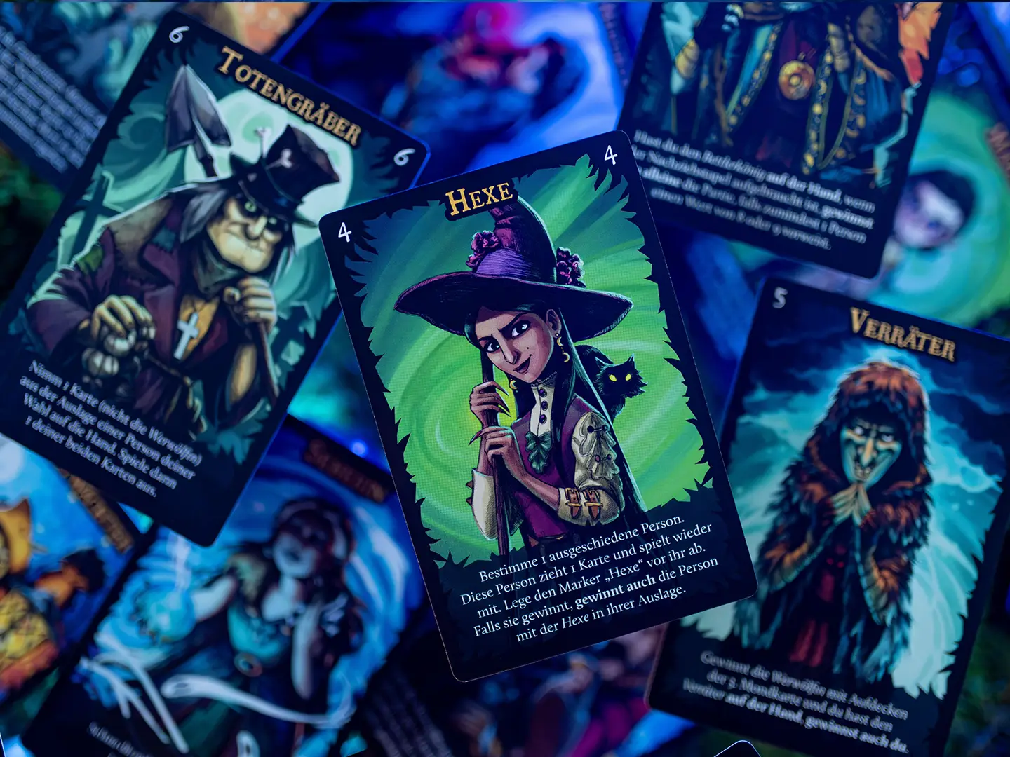 Nahaufnahme von Spielkarten aus Wolfsmond mit den illustrierten Figuren Totengräber, Hexe und Verräter in dunklen Blau-, Grün- und Violetttönen.